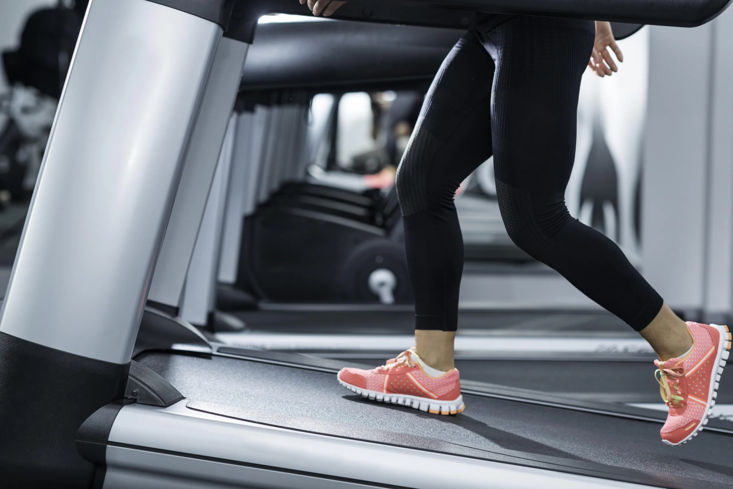 Photo of the bottom half of woman walking on the treadmill at an incline. Her sneakers are pink and lime green, with black athletic pants on.